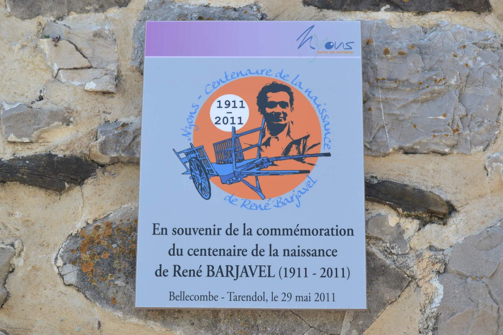 Plaque de la ville de Nyons posée à Bellecombe-Tarendol pour le centenaire de la naissance de René Barjavel, avec son portrait et une charrette bleue
