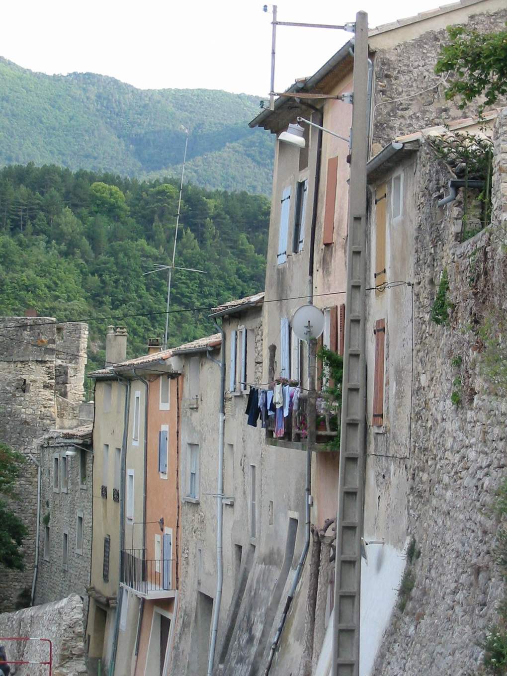 Façades d'une rue du vieux Nyons, avec une colline couverte de pins et de chênes juste derrière les toits